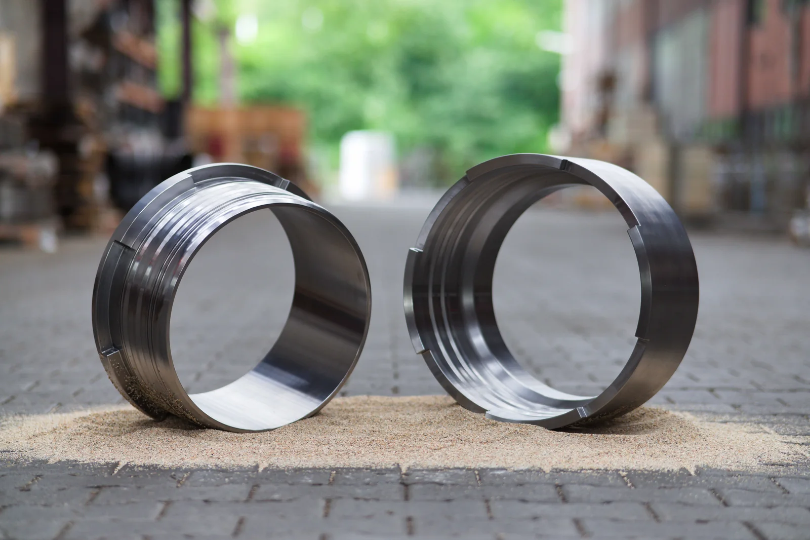 Two machined ZSM steel coupling rings standing upright on sand in the works yard, the circumferential grooves and locking slots visible on their rims